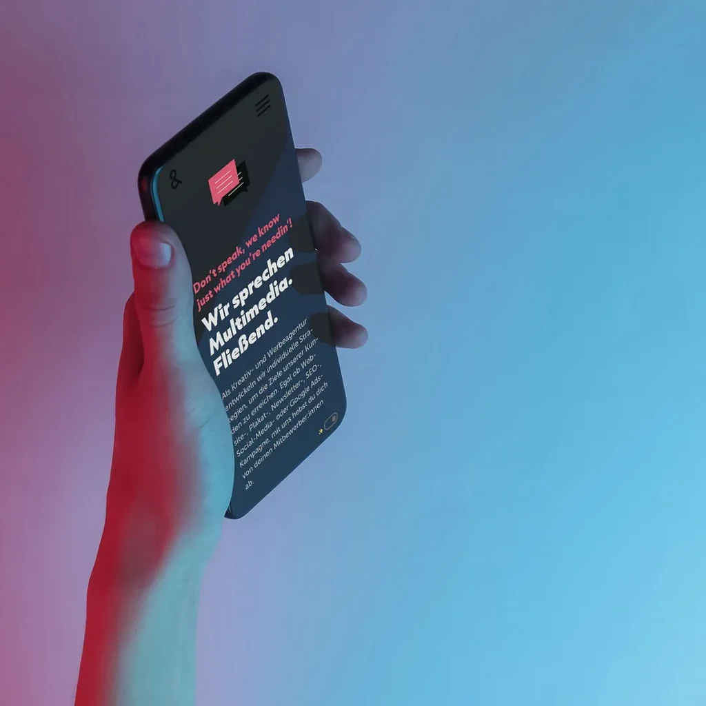 Eine Hand hält ein Smartphone auf der die Kopf & Hand Website im Darkmode angezeigt wird. Der HIntergrund ist dunkel, pink-blau leicht beleuchtet